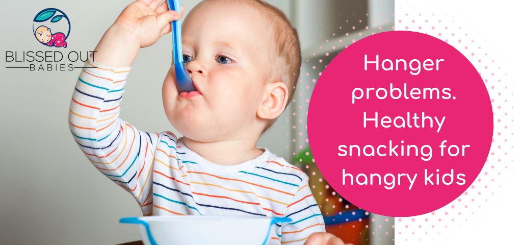 Image of baby feeding himself with a spoon. Blog about Hangry babies and how to give them healthy snacks.